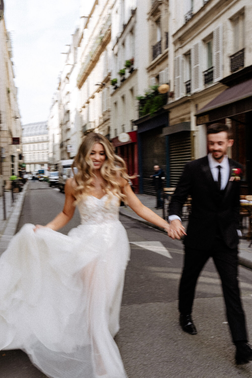 paris elopement planner - bride and groom hold hand running on street of paris